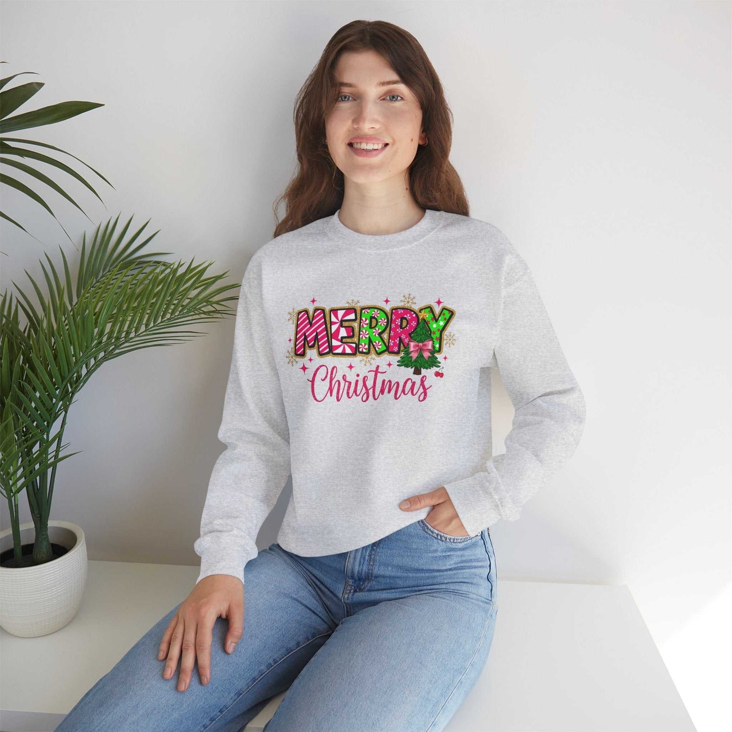 woman wearing gray Merry Christmas Candy Cane typography sweatshirt sitting indoors near potted plant