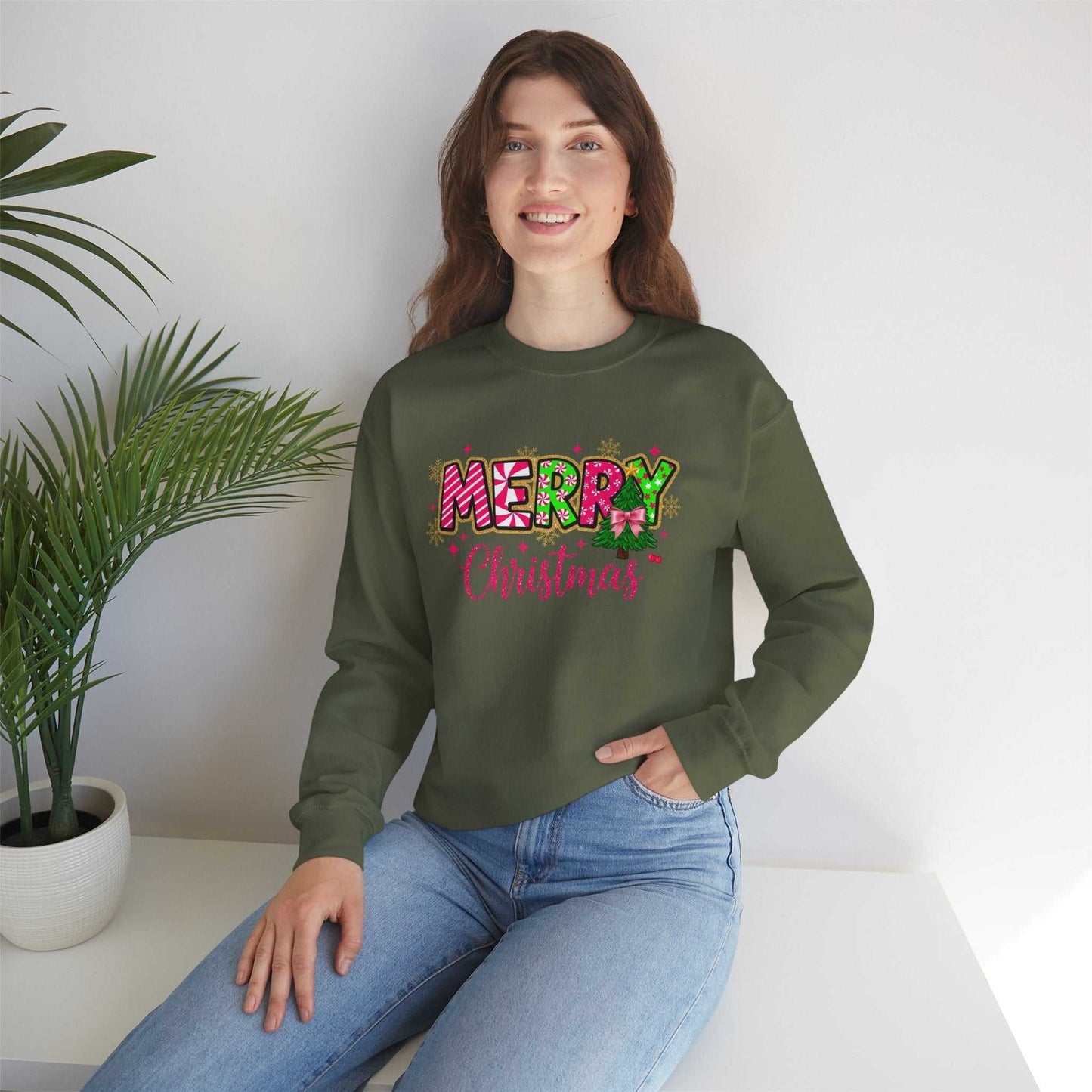 Woman wearing green Merry Christmas Candy Cane typography sweatshirt sitting by white table with plant