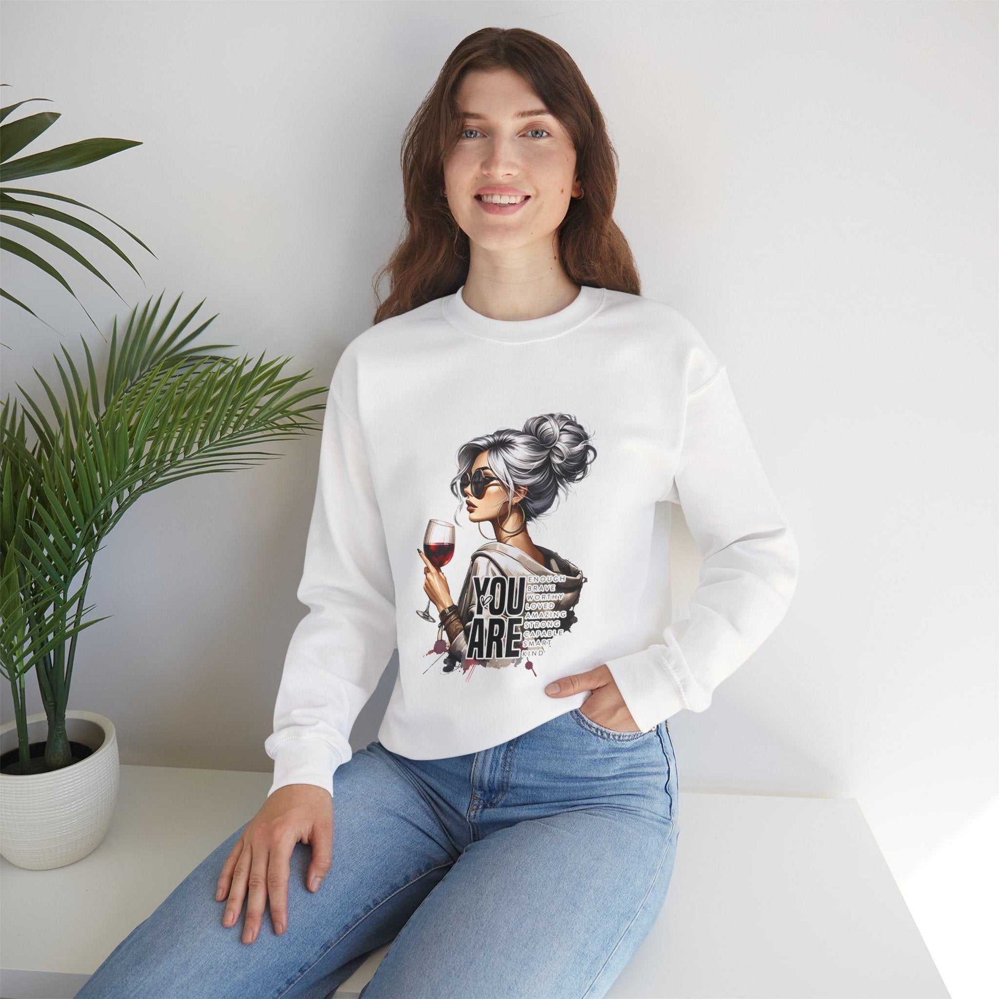 Chic woman with silver hair wearing white crewneck sweatshirt holding wine glass with "You Are Loved" text