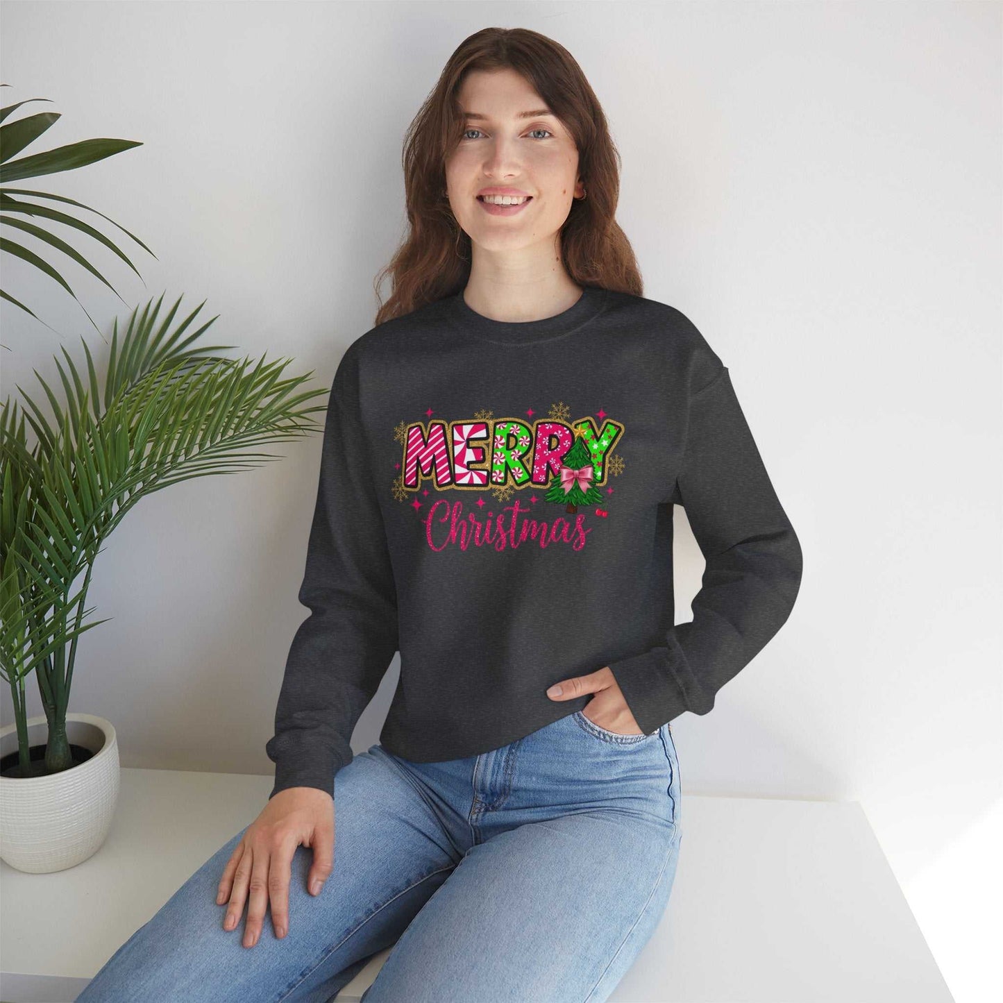 woman wearing black Merry Christmas Candy Cane typography sweatshirt sitting indoors with palm plant in background