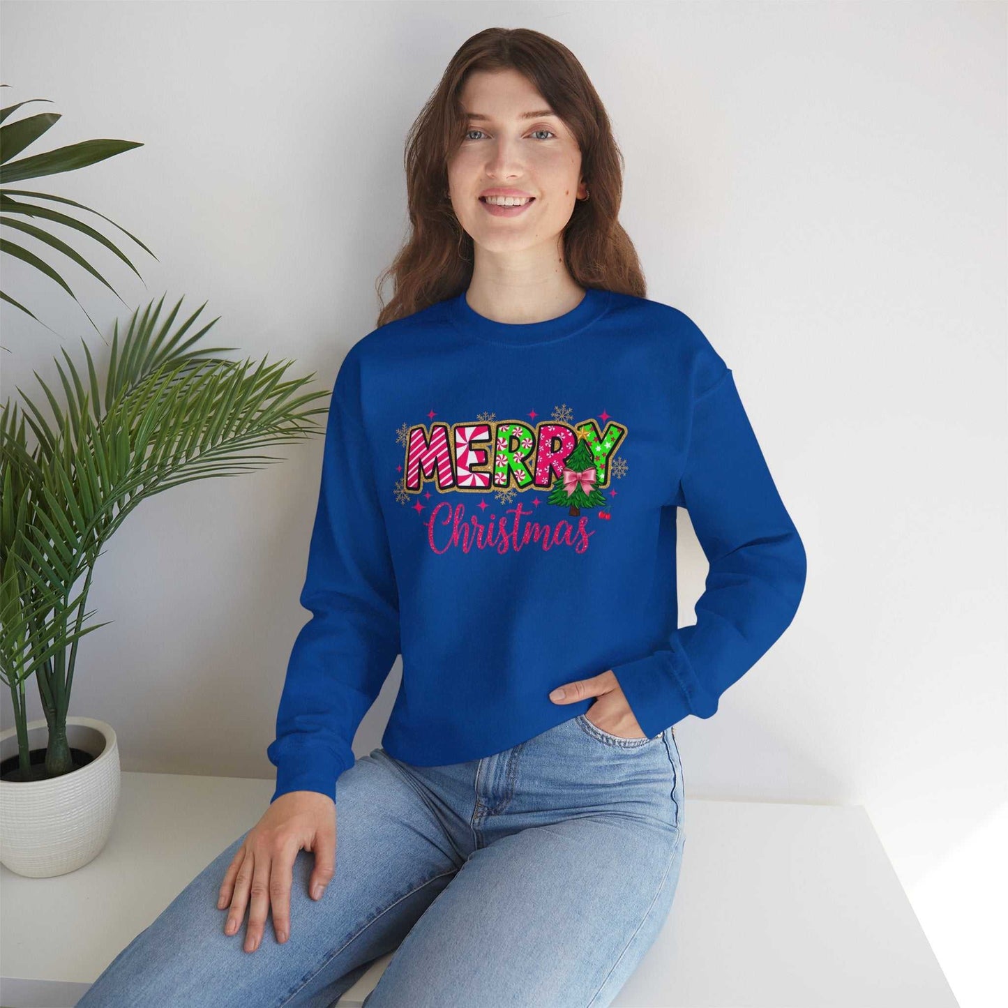 woman wearing blue crewneck sweatshirt with colorful Merry Christmas Candy Cane typography design sitting indoors