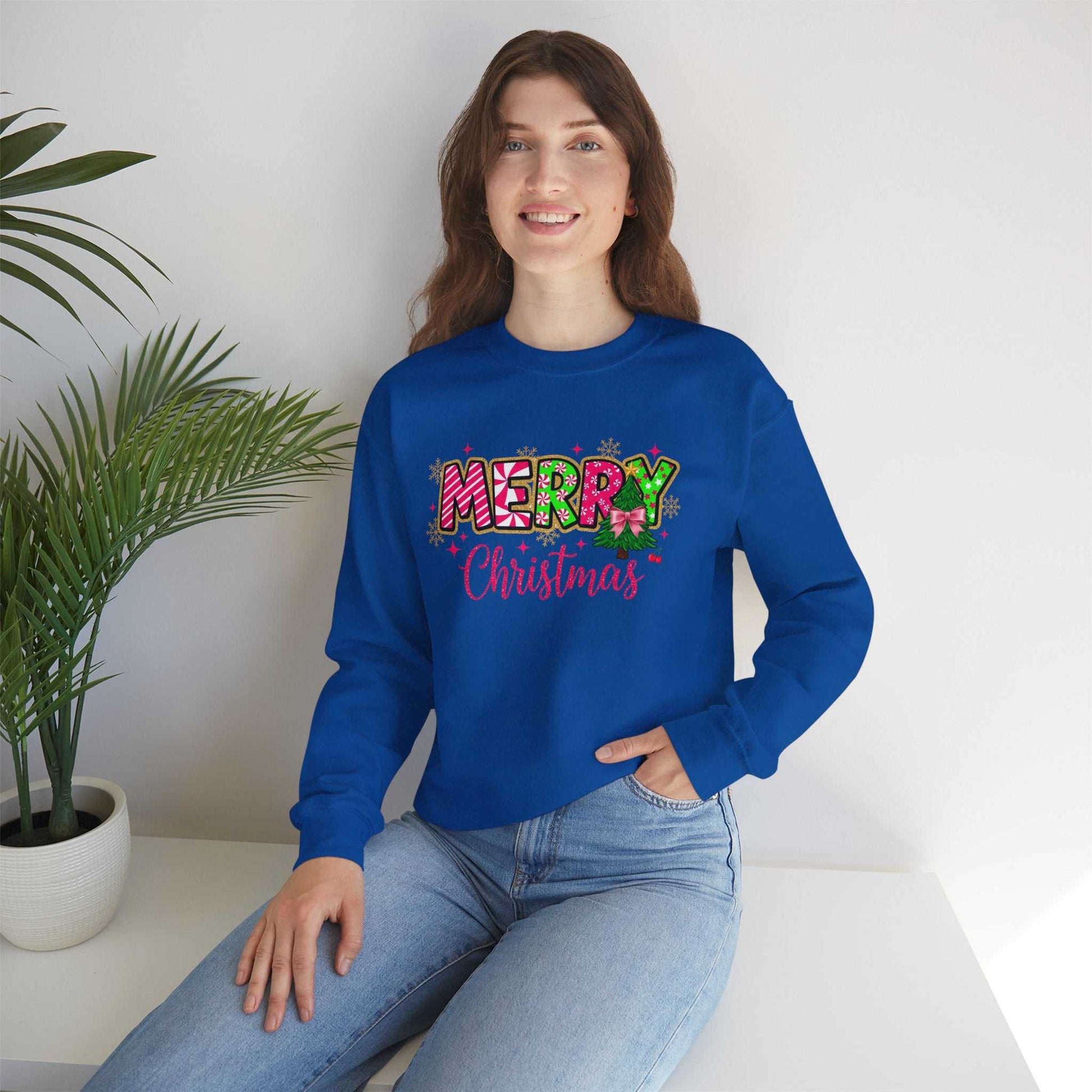 woman wearing blue crewneck sweatshirt with colorful Merry Christmas Candy Cane typography design sitting indoors