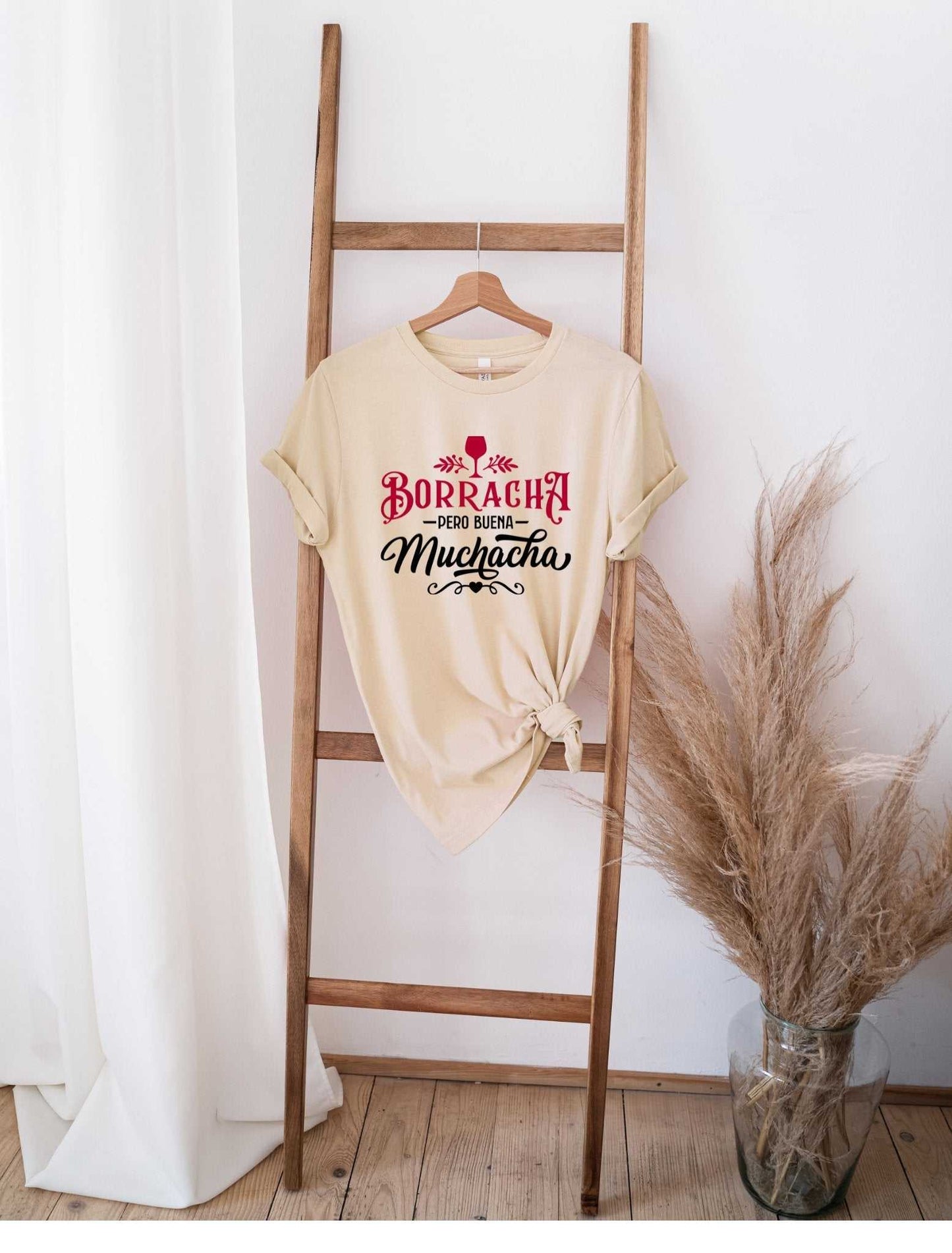 Borracha pero buena muchacha graphic t-shirt hanging on wooden ladder with dried pampas grass decor