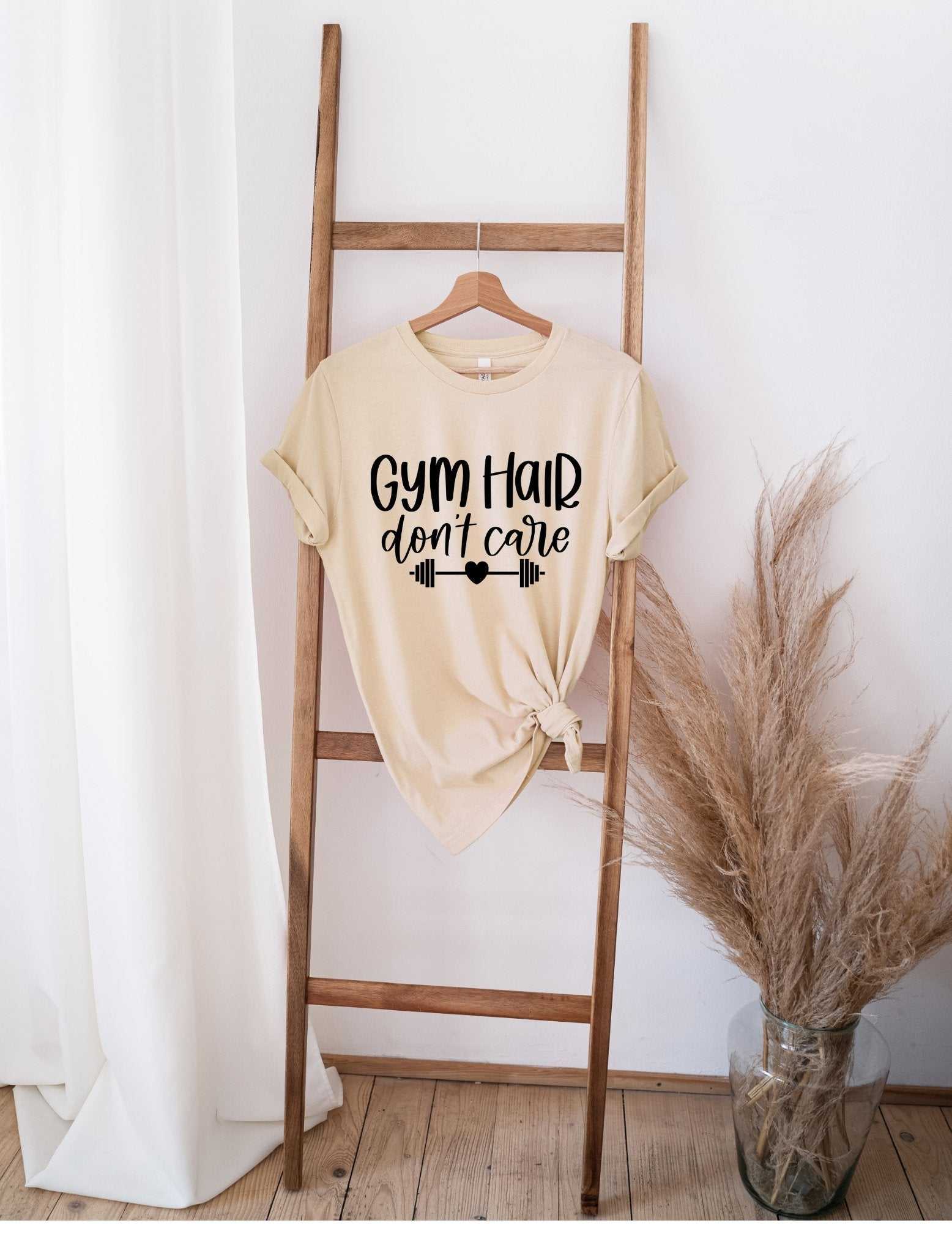 Beige GYM Hair Don't Care t-shirt hanging on wooden ladder with pampas grass decor