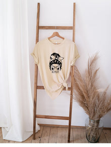 Beige Messy Bun GYM Life t-shirt with graphic print hanging on wooden ladder next to dried pampas grass.
